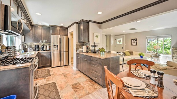 A modern kitchen with dark cabinetry, stainless steel appliances, and a dining area with a wooden table set for four. - Family-friendly Kirkland Home ~ 1 Mi to Downtown (Kirkland)