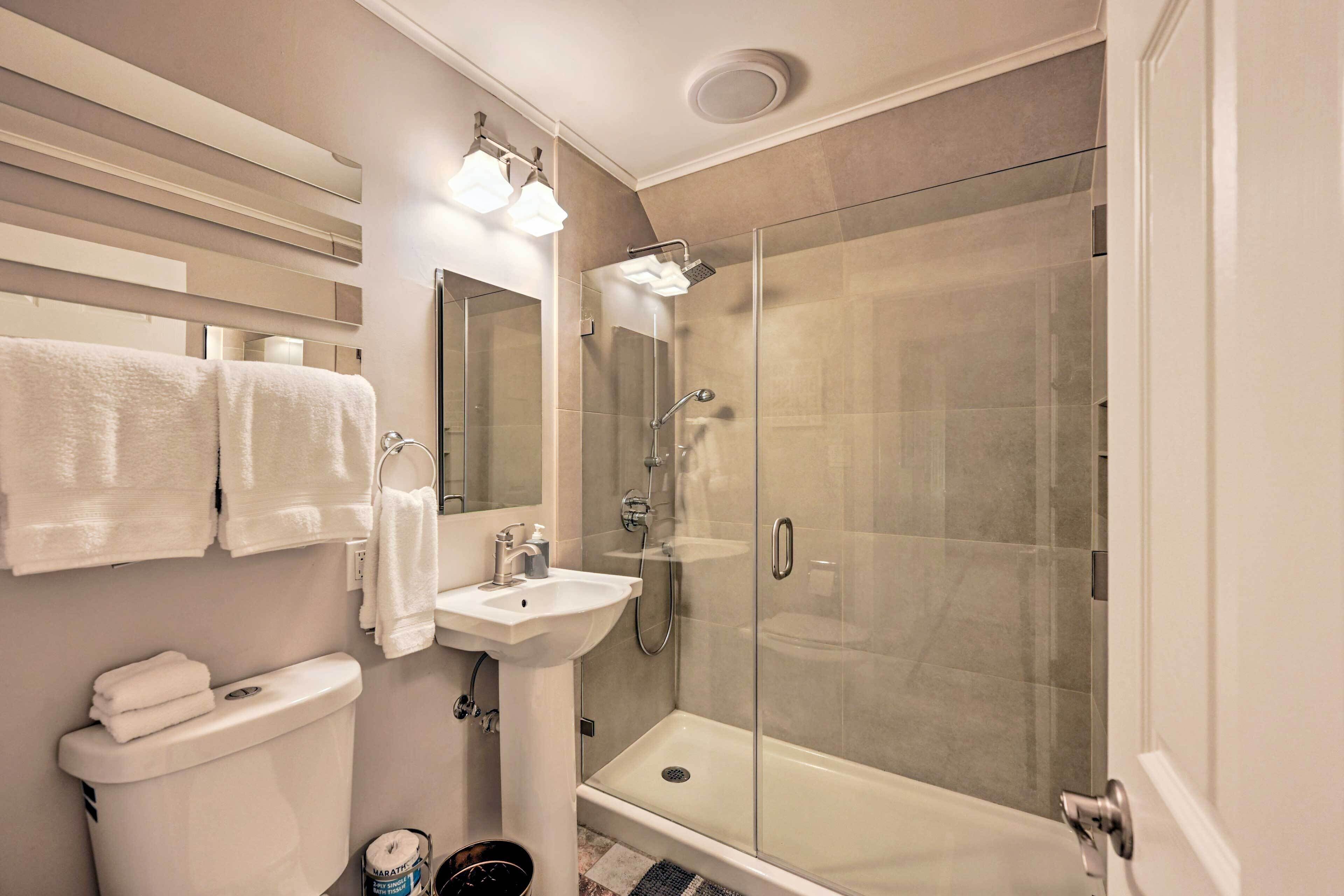 Un baño moderno con ducha envuelta en vidrio, un lavamanos blanco y un inodoro.
