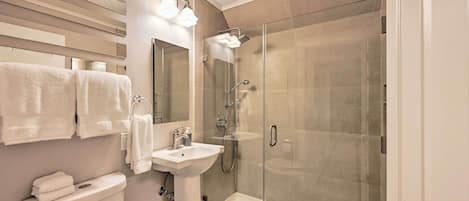 Un baño moderno con ducha envuelta en vidrio, un lavamanos blanco y un inodoro.