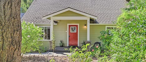 A house with a red door, a small porch, and a garden with various plants.