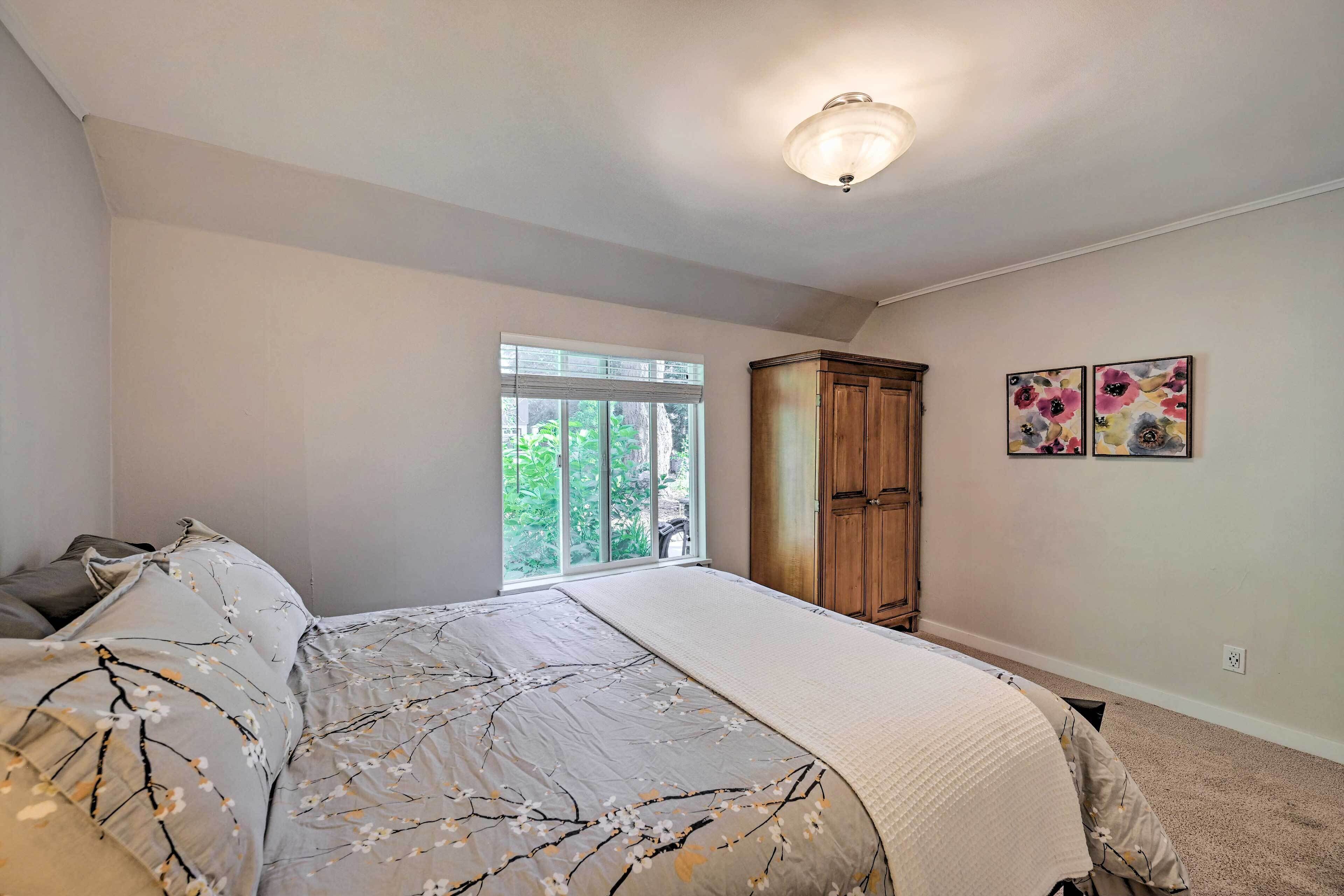 A bedroom with a large bed, a window, a wardrobe, and two floral paintings on the wall.