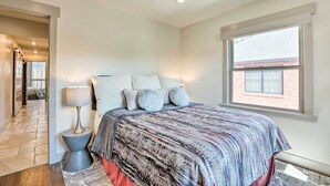 Un dormitorio con cama, almohadas, lámpara, ventana y puerta que da a otra habitación.