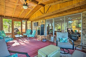 Un espace extérieur abrité, doté de poutres en bois, d’un ventilateur de plafond et d’une grande porte-fenêtre coulissante donnant sur un patio.