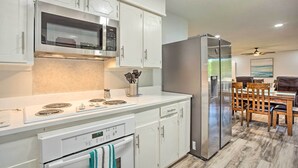 A modern kitchen with white cabinetry, a stainless steel refrigerator, and a dining area with wooden chairs and a table. - Cedar Creek Lake Home: Private Dock & Hot Tub (Mabank)