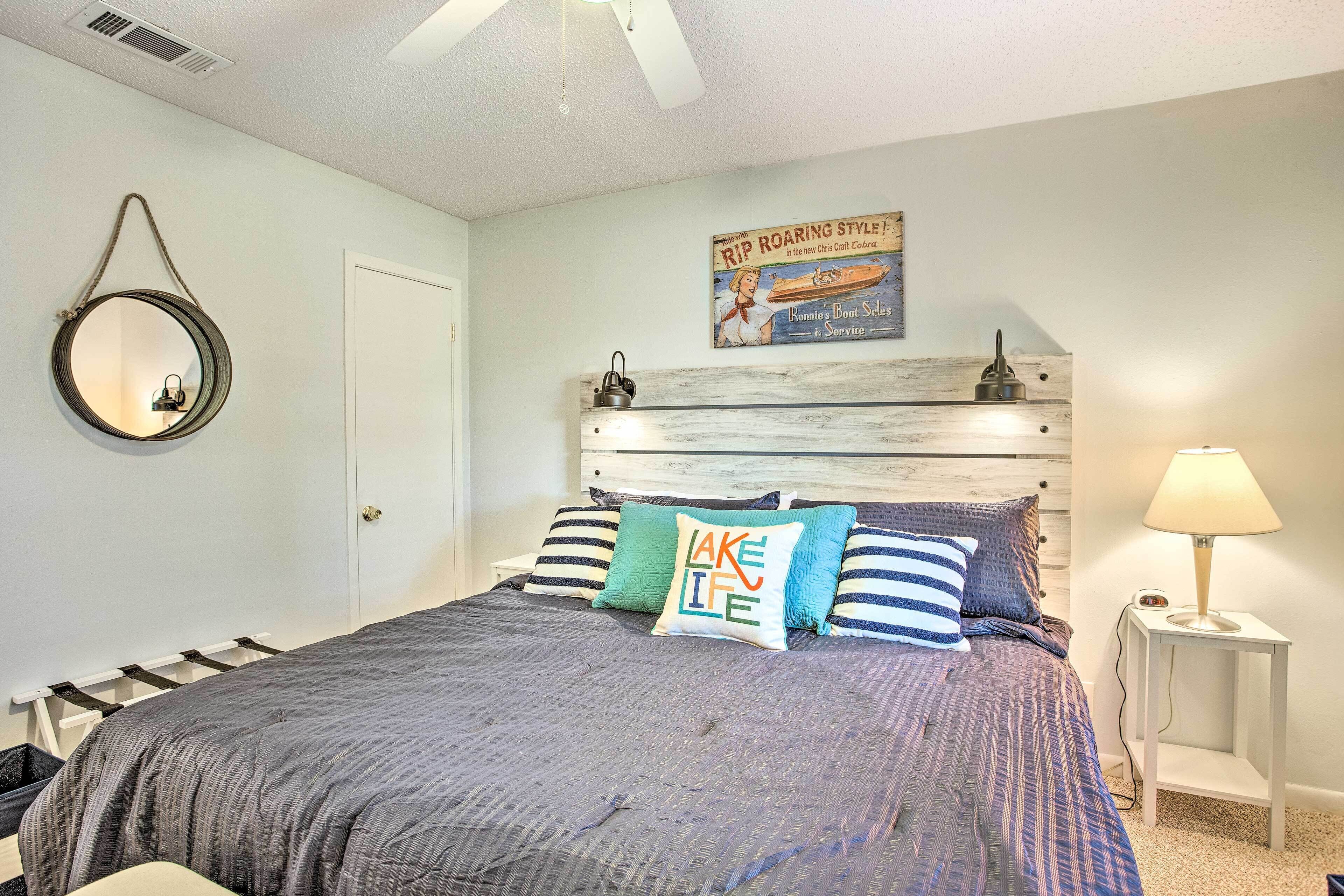 A bedroom with a bed, a bedside table with a lamp, a wall-mounted mirror, and a poster on the wall.