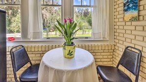 Une pièce avec une table ronde, deux chaises, une plante en pot et un tableau accroché au mur.