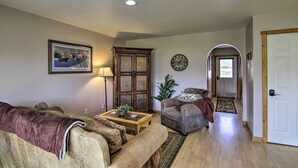A living room with a sofa, armchair, and a wooden cabinet. There is a lamp, a clock, and a door leading to another room.