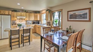 A modern kitchen with wooden cabinets, a central island, and a dining area with a large wooden table and chairs.