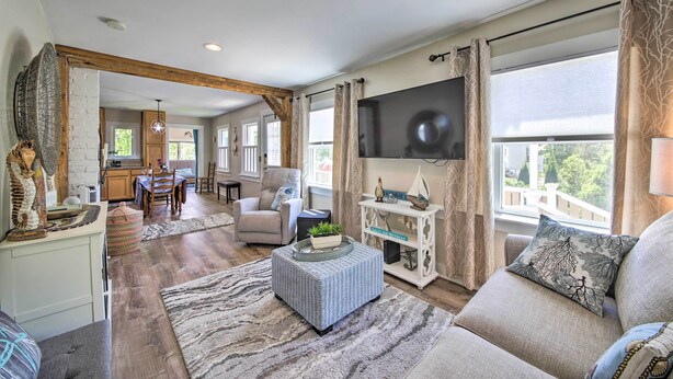 A spacious living room with a large TV, comfortable seating, a dining area, and a kitchen in the background. - Charming East Boothbay Cottage w/ Large Yard! (East Boothbay)