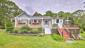 A two-story house with a covered porch, a small deck, and a staircase leading to the upper level. - Charming East Boothbay Cottage w/ Large Yard! (East Boothbay)