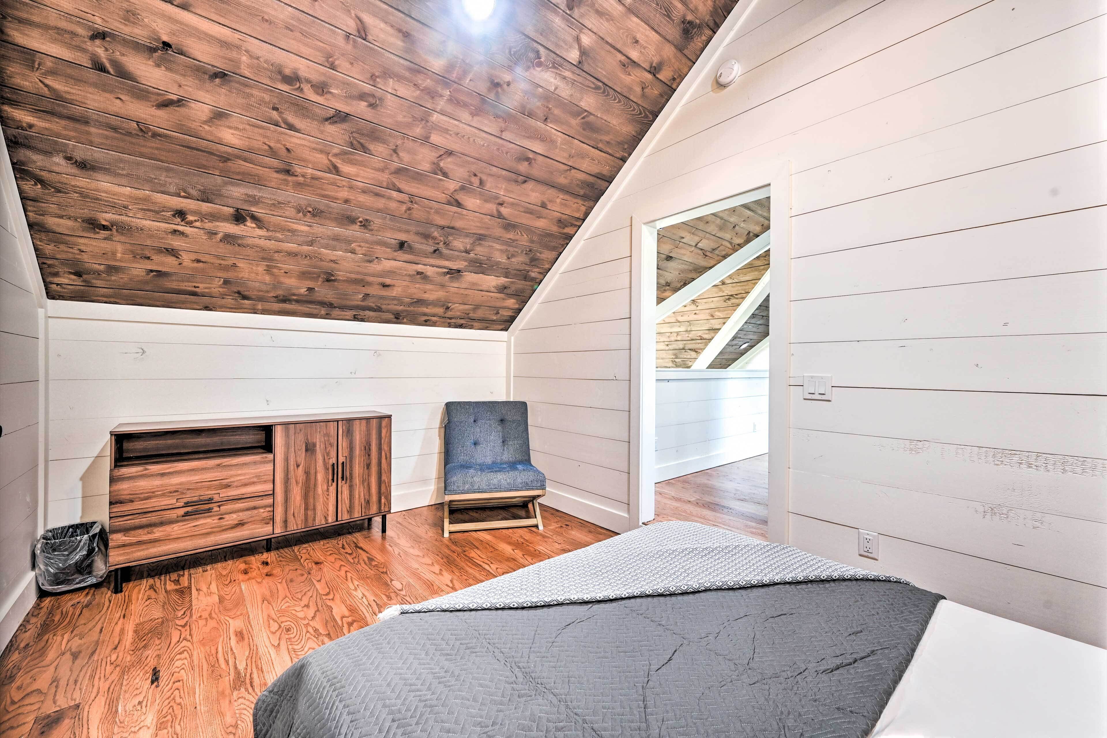 Un dormitorio con techo inclinado, piso de madera, cama, una silla y armario empotrado.