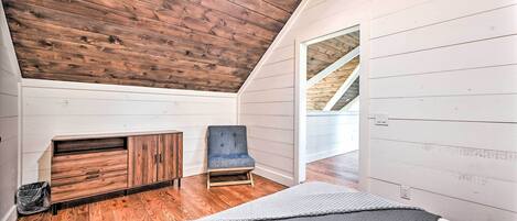 A bedroom with a sloped ceiling, wooden flooring, a bed, a chair, and a built-in wardrobe.
