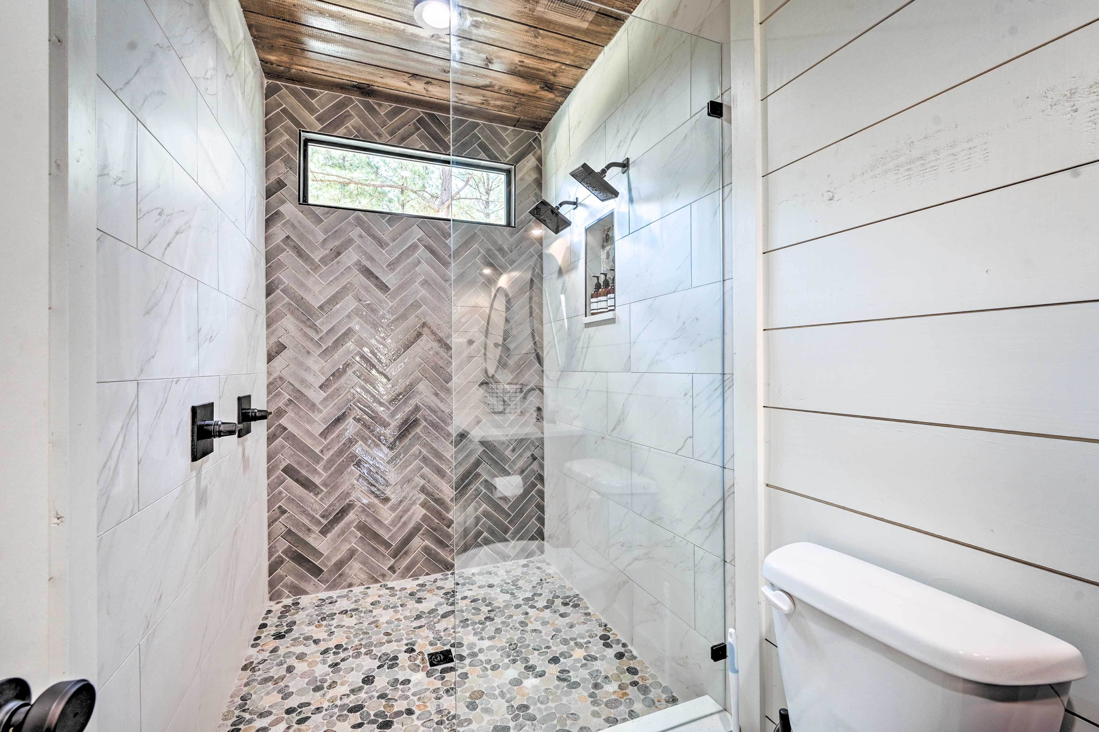 A bathroom with a herringbone tile wall, a shower with a glass door, and a toilet.
