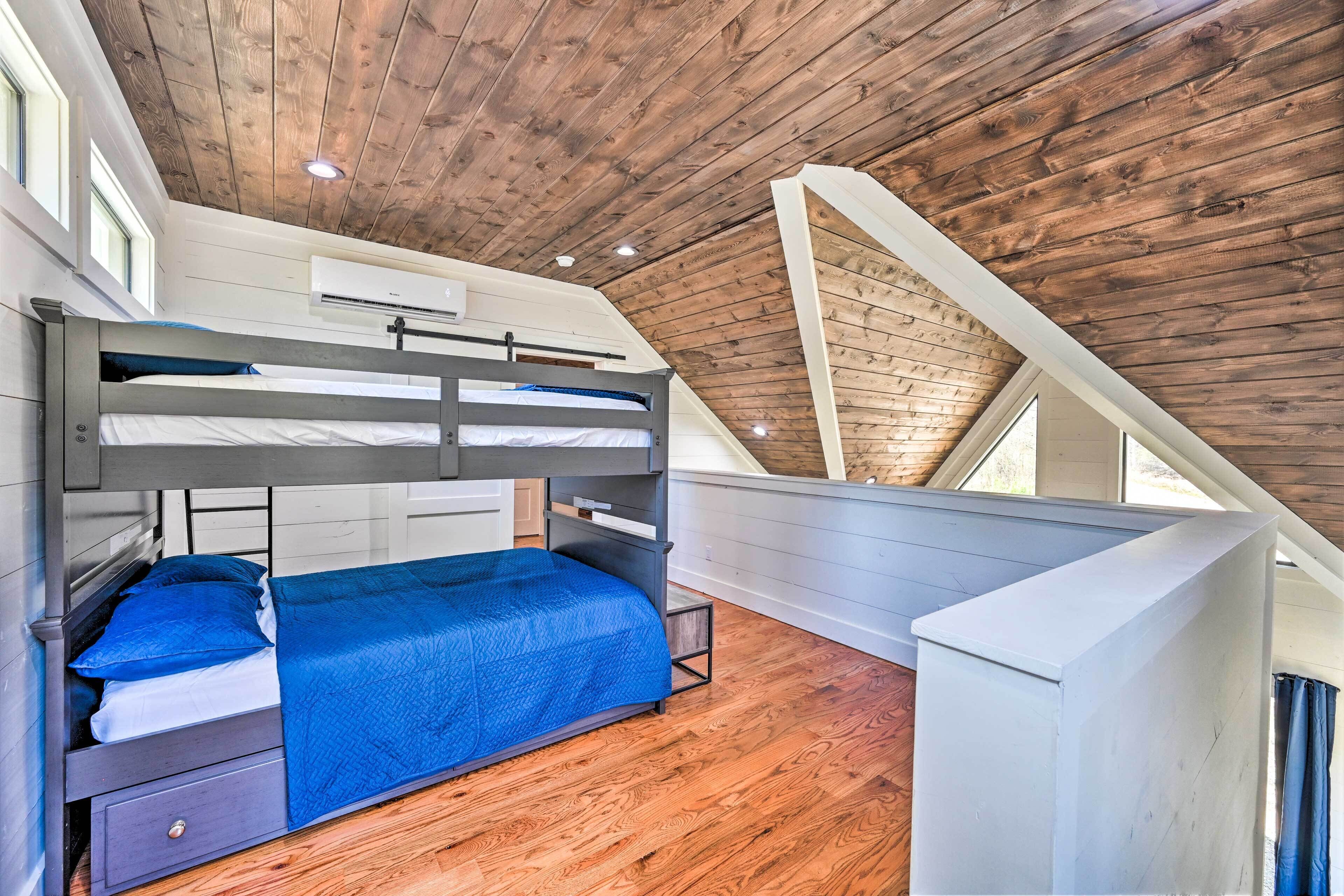 A bunk bed with a blue bedspread in a room with wooden flooring and a sloped ceiling.