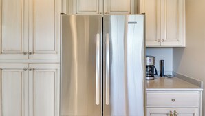 A kitchen with white cabinetry, a stainless steel refrigerator, and a coffee maker on the countertop. - Stunning Lakeside House w/ Deck + Water Views (Lakeside)
