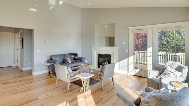 A spacious living room with a fireplace, a balcony with a railing, and a large window providing a view of trees. - Stunning Lakeside House w/ Deck + Water Views (Lakeside)
