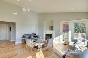 Un salon spacieux avec une cheminée, un balcon doté d’une balustrade et une grande fenêtre offrant une vue sur les arbres.