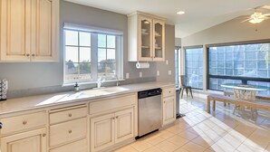 A modern kitchen with a dishwasher, double sink, and a dining area with a table and chairs. - Stunning Lakeside House w/ Deck + Water Views (Lakeside)