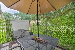 A patio with a table and chairs under a large umbrella, surrounded by a white fence and lush greenery. - Renovated Kissimmee Townhome: 5 Mi to Disney! (Kissimmee)