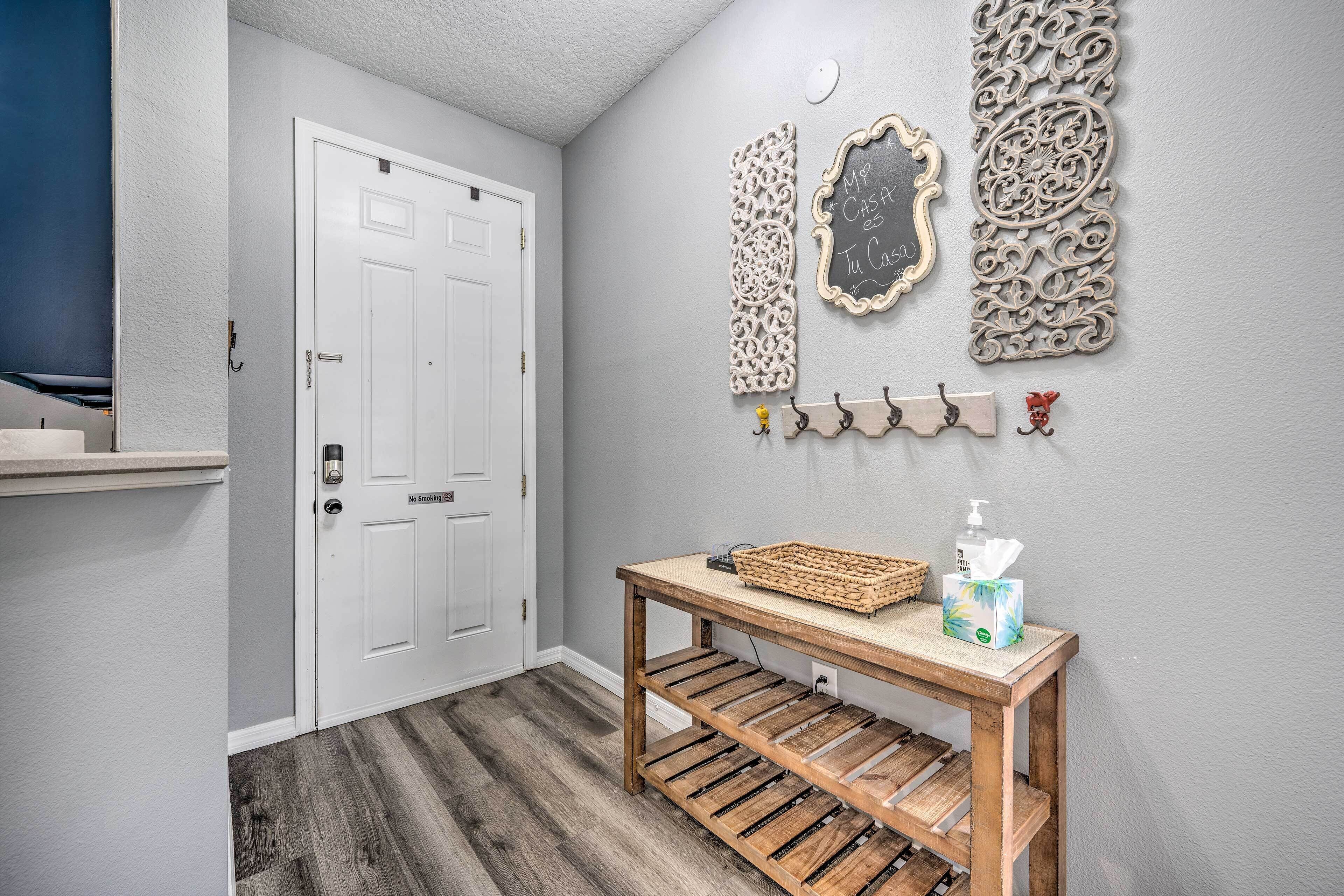 A hallway with a white door, a wooden bench with a basket and tissues, and decorative wall art.