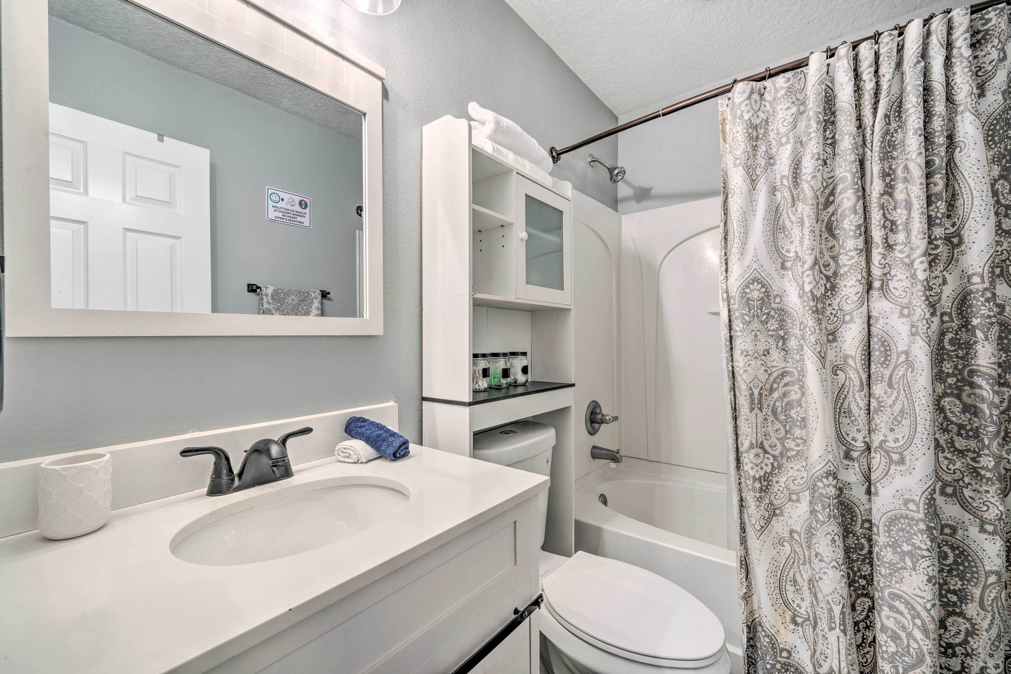 A bathroom with a white sink, mirror, and toilet, a shower curtain, and a towel rack.