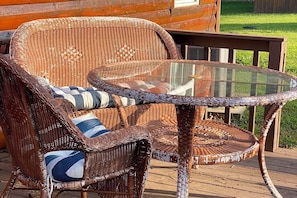 Mobiliario de mimbre con cojines, una mesa con superficie de vidrio y una terraza de madera.