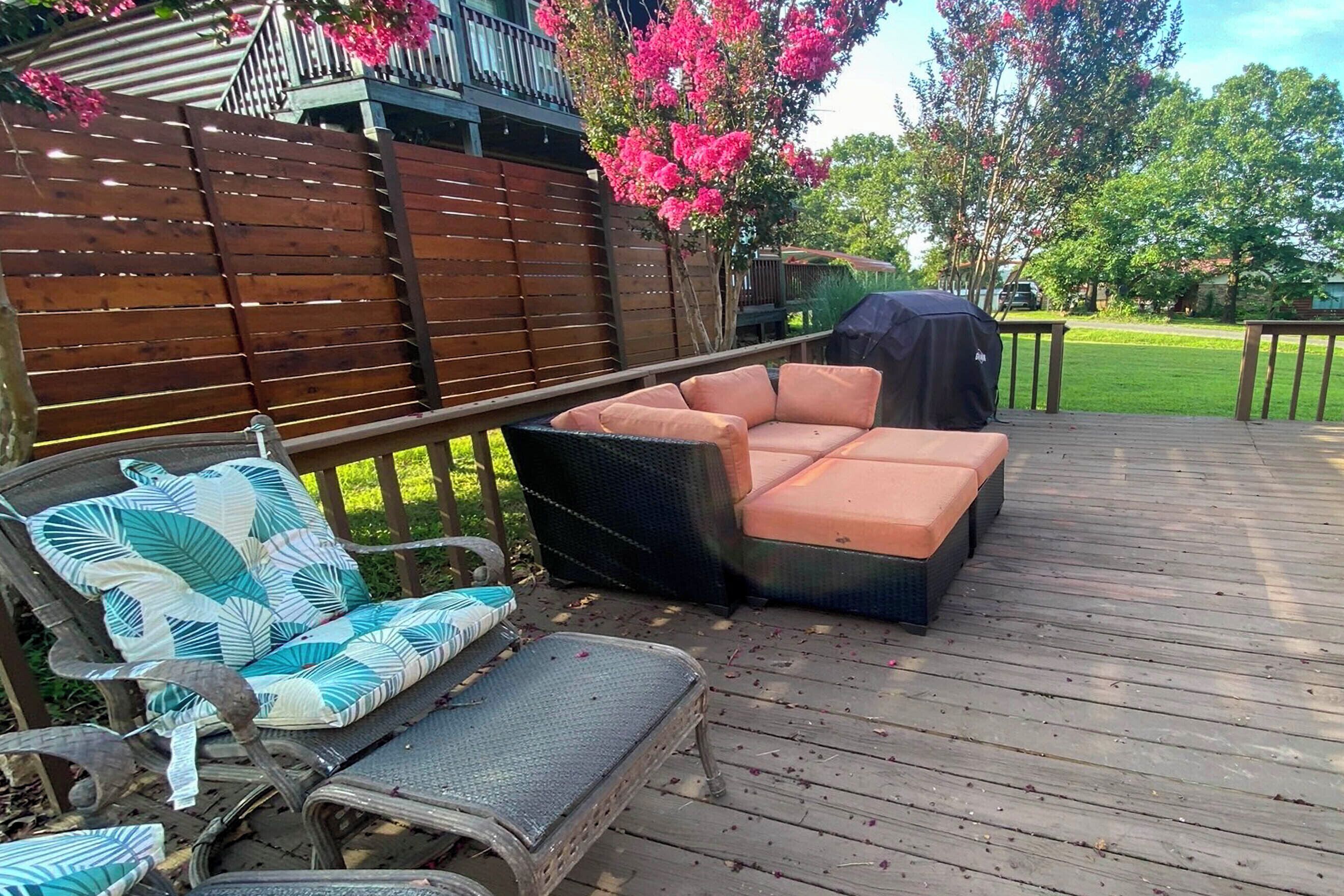 Terraza de madera con mobiliario exterior, incluyendo un sofá, sillas y una parrilla.