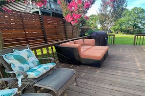 Terraza de madera con mobiliario exterior, incluyendo un sofá, sillas y una parrilla.