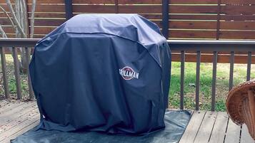 A grill with a brand logo, placed on a mat on a wooden deck.