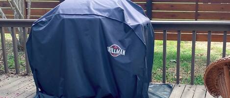 A grill with a brand logo, placed on a mat on a wooden deck.