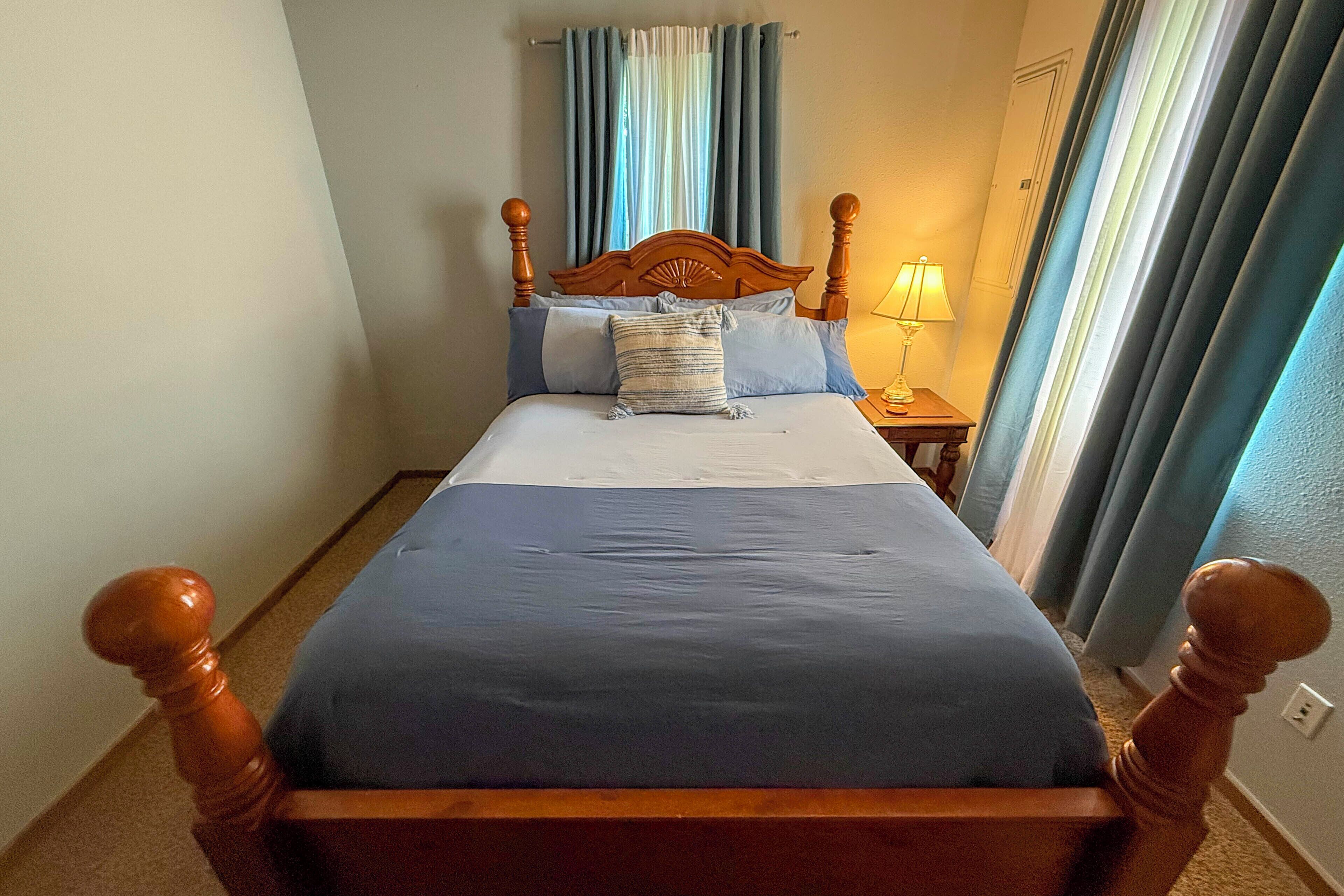 A bed with a wooden headboard, a nightstand with a lamp, and a window with curtains.