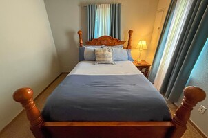 Una cama con cabecera de madera, una mesita de noche con lámpara y una ventana con cortinas.