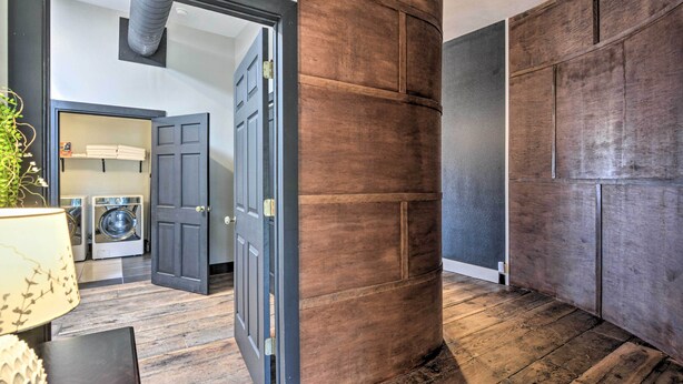 A room with a wooden floor, a large wooden panel wall, and a door leading to a laundry area with washing machines. - Upscale Loft in the Heart of Dtwn Springfield (Springfield)