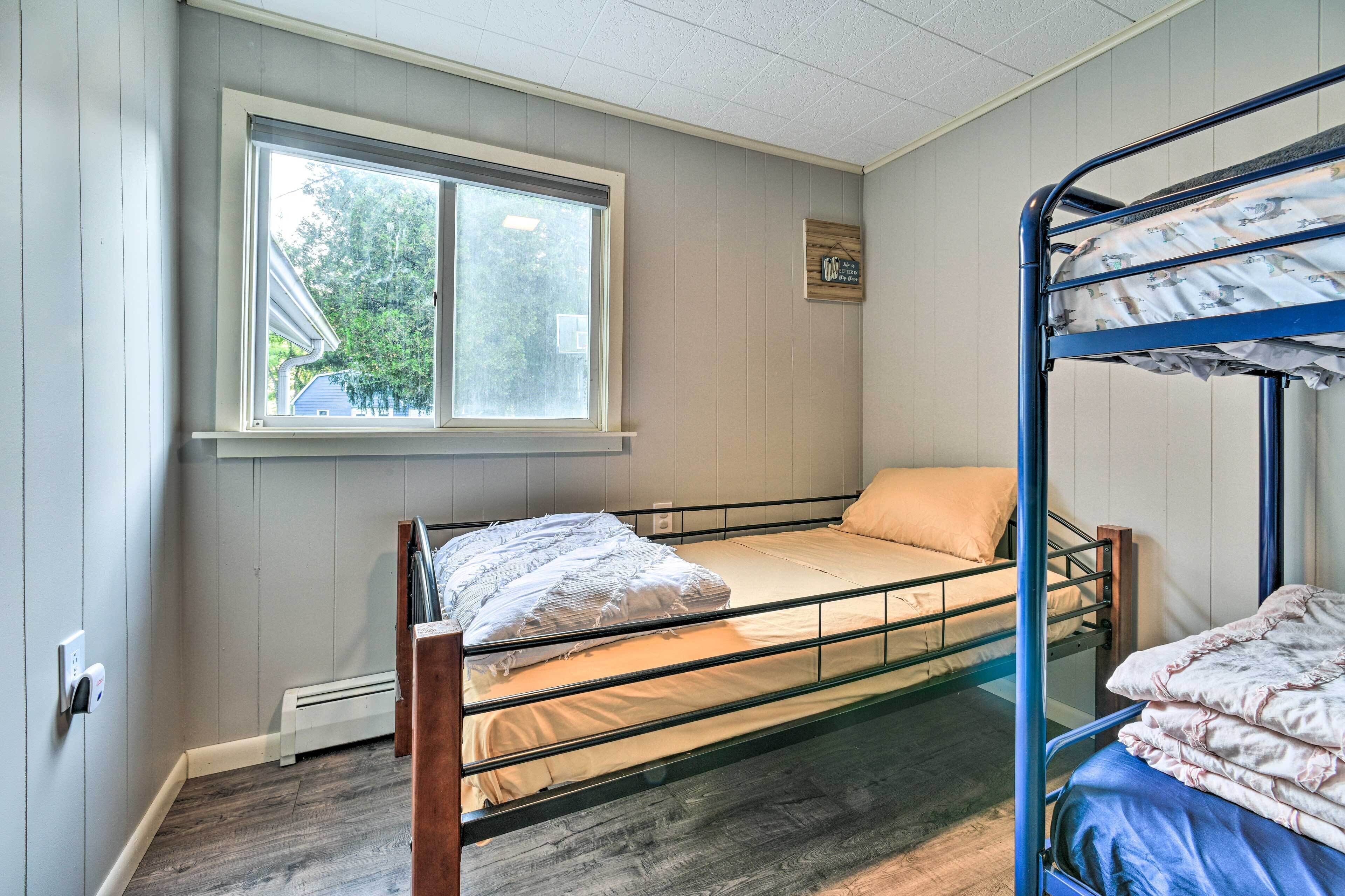 A dormitory room with bunk beds, a window, and a thermostat on the wall.
