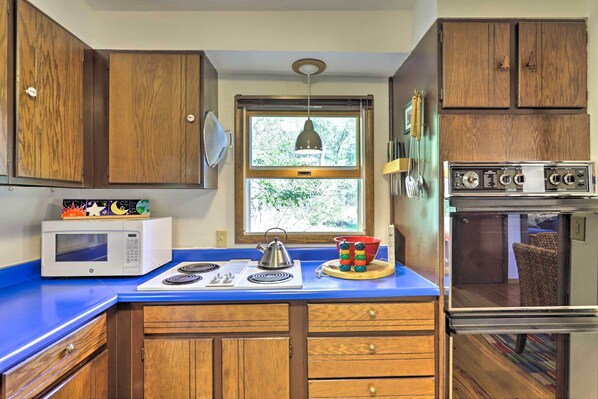 A kitchen with wooden cabinets, a microwave, a stove, and a window with a view of trees.