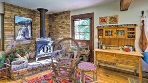 A rustic interior with a brick fireplace, a wooden table, a wicker chair, and a bookshelf. - Cabin in Beautiful Setting Between Ouray & Ridgway (Ridgway)
