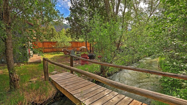 A wooden bridge over a stream with a wooden deck, surrounded by lush greenery and a wooden fence in the background. - Cabin in Beautiful Setting Between Ouray & Ridgway (Ridgway)