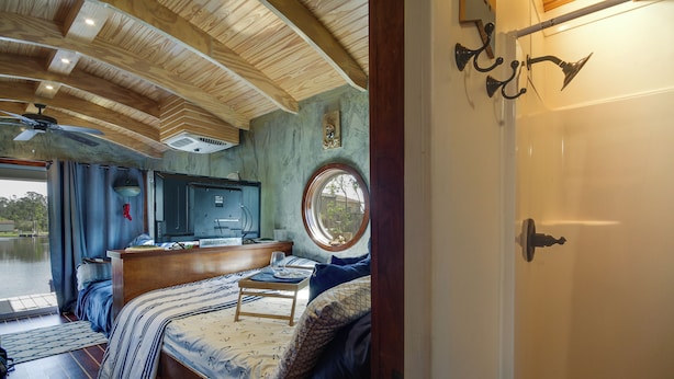 A cozy cabin interior with a bed, a small table, a TV, and a window overlooking a natural landscape. - Bay St Louis Houseboat 6 Mi to Old Town & Beach! (Bay St Louis)