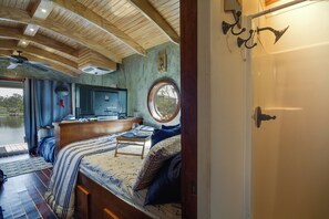 Interior acogedor de una cabaña con una cama, una mesita, un televisor y una ventana con vistas a un paisaje natural.