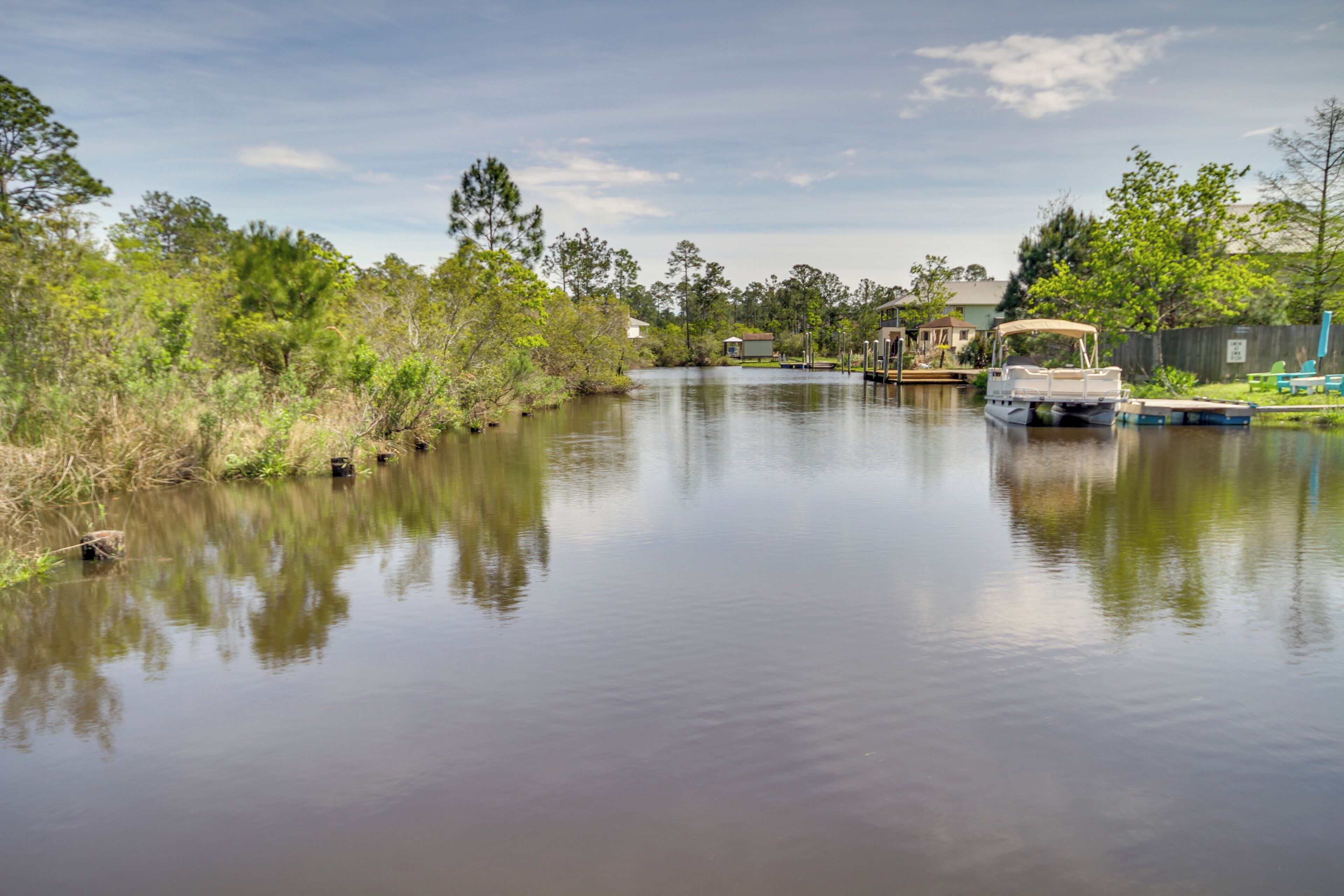 Une rivière paisible, bordée de bateaux, de verdure et de maisons.