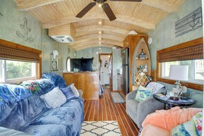 Un interior acogedor con techo de madera, una zona de cocina y un espacio de sala con sofá y mesa.