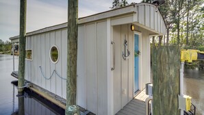 A small, white docked houseboat with a blue door, a small window, and a deck. - Bay St Louis Houseboat 6 Mi to Old Town & Beach! (Bay St Louis)