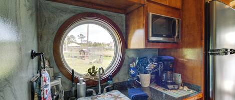 Cocina compacta con armarios de madera, un refrigerador de acero inoxidable, un microondas y una ventana con vistas al exterior.