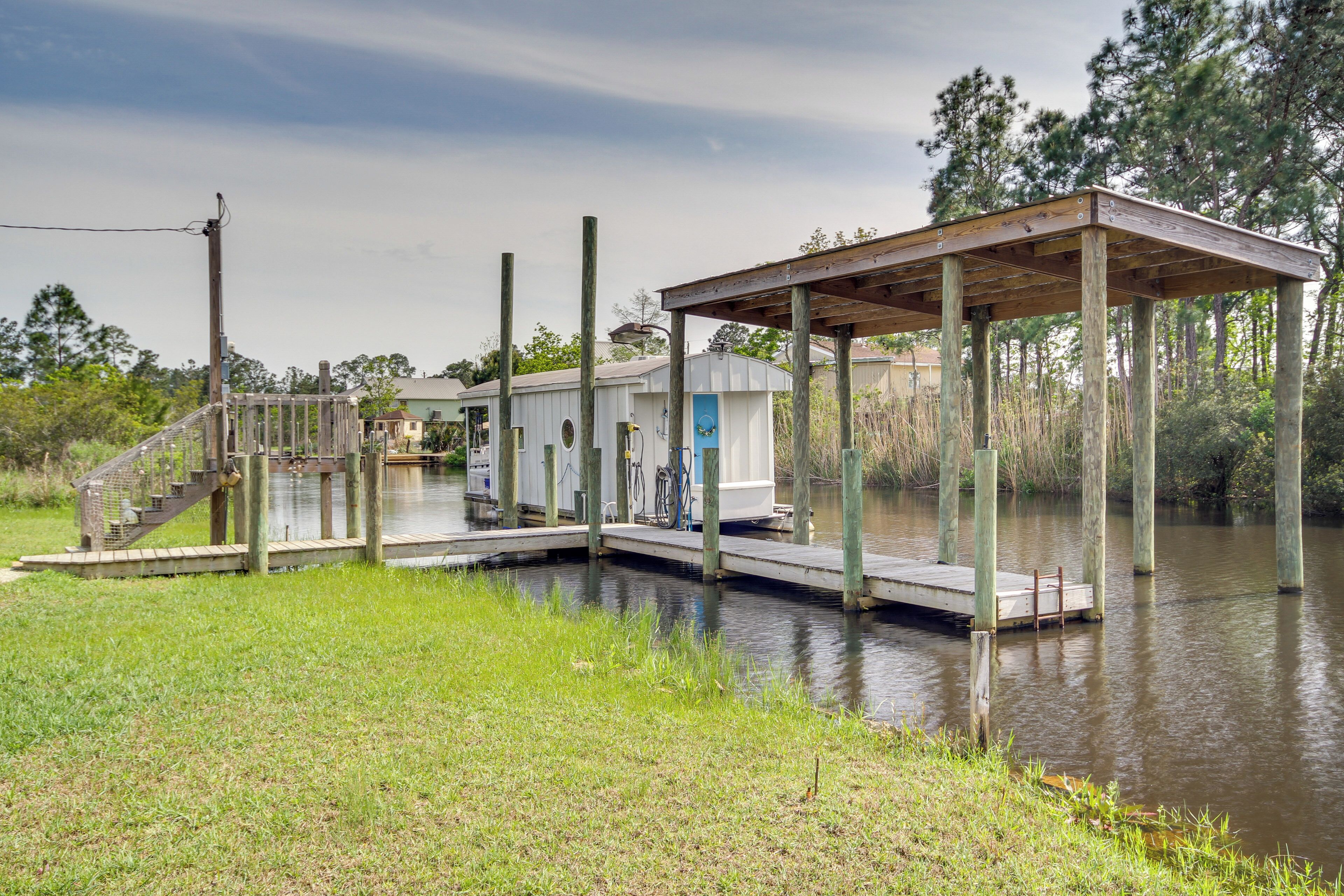 A dock extending into a body of water with a covered structure and a small building with a blue door.