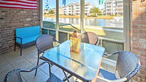 An outdoor patio with a glass table, wicker chairs, and a blue bench. - Screened Porch + Golf On-site: Myrtle Beach Condo (Myrtle Beach)