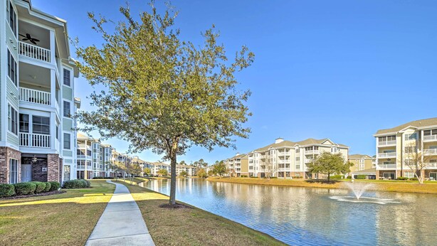 A residential area with multi-story buildings, a water body, and a tree-lined pathway. - Screened Porch + Golf On-site: Myrtle Beach Condo (Myrtle Beach)