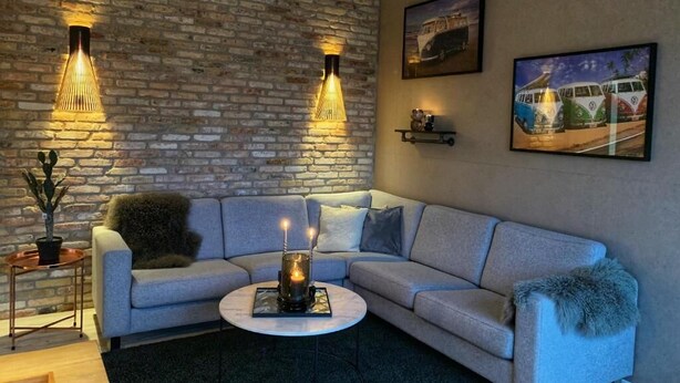 Ein modernes Wohnzimmer mit Backsteinwand, einem Ecksofa, einem runden Couchtisch und zwei Wandleuchten.