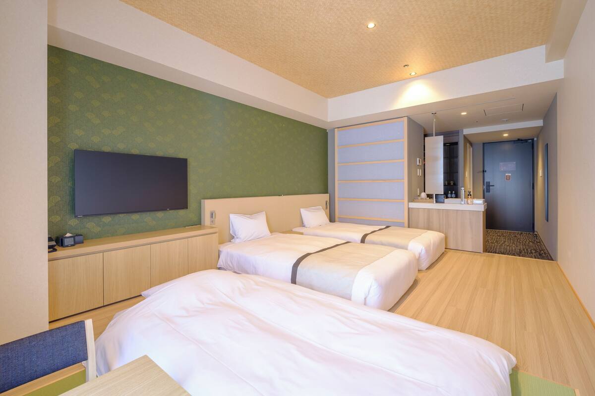 A hotel room with three beds, a flat-screen TV, a desk, and a mirror.