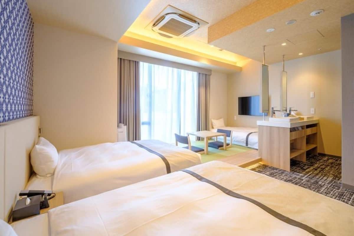 A hotel room with two beds, a desk, a TV, and a bathroom.