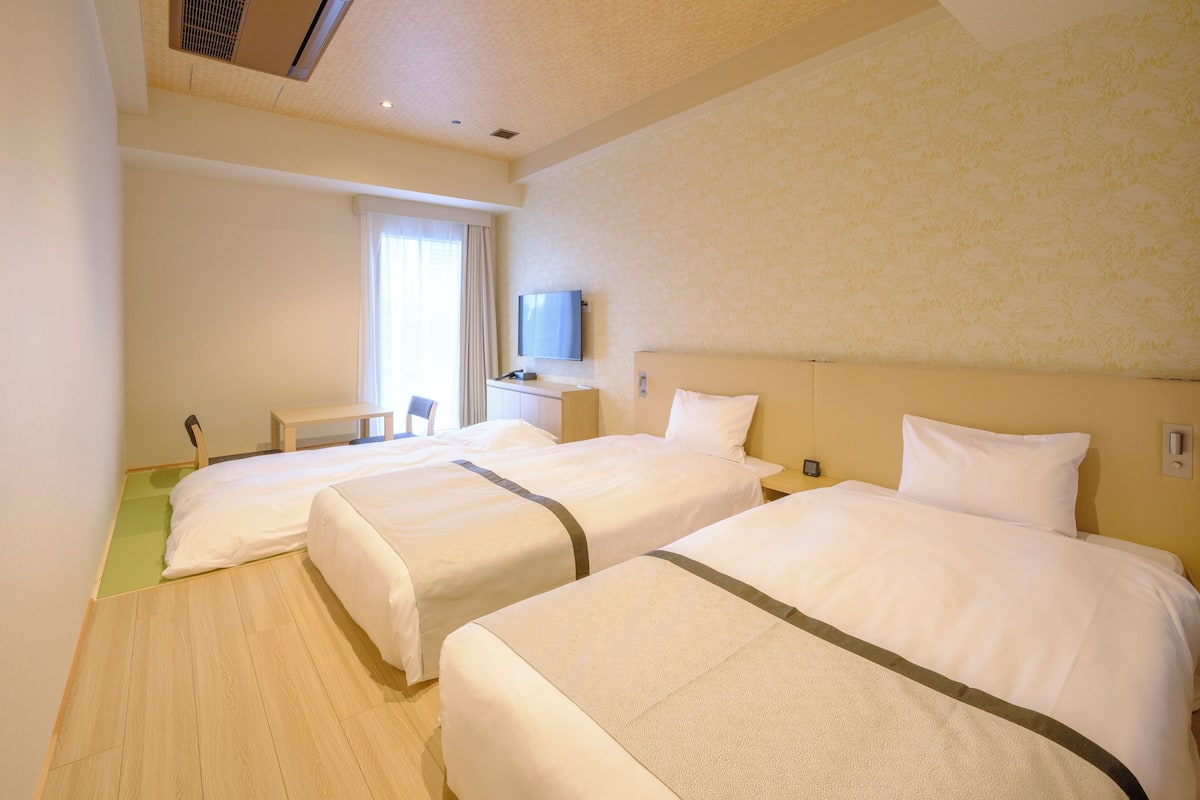 A hotel room with two beds, a desk, a chair, and a television on the wall.